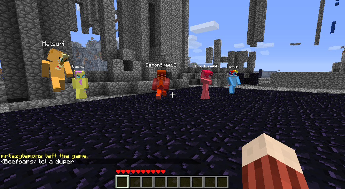 A group of players standing in a large, open area with a blue sky and gray stone blocks. The players are wearing different colored outfits and have various items in their hands.