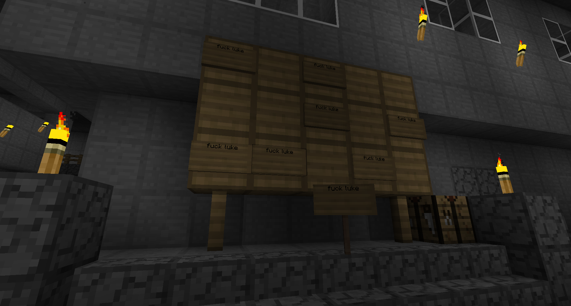 A large wooden sign with many names on it, in a dark room with stone walls and floors.