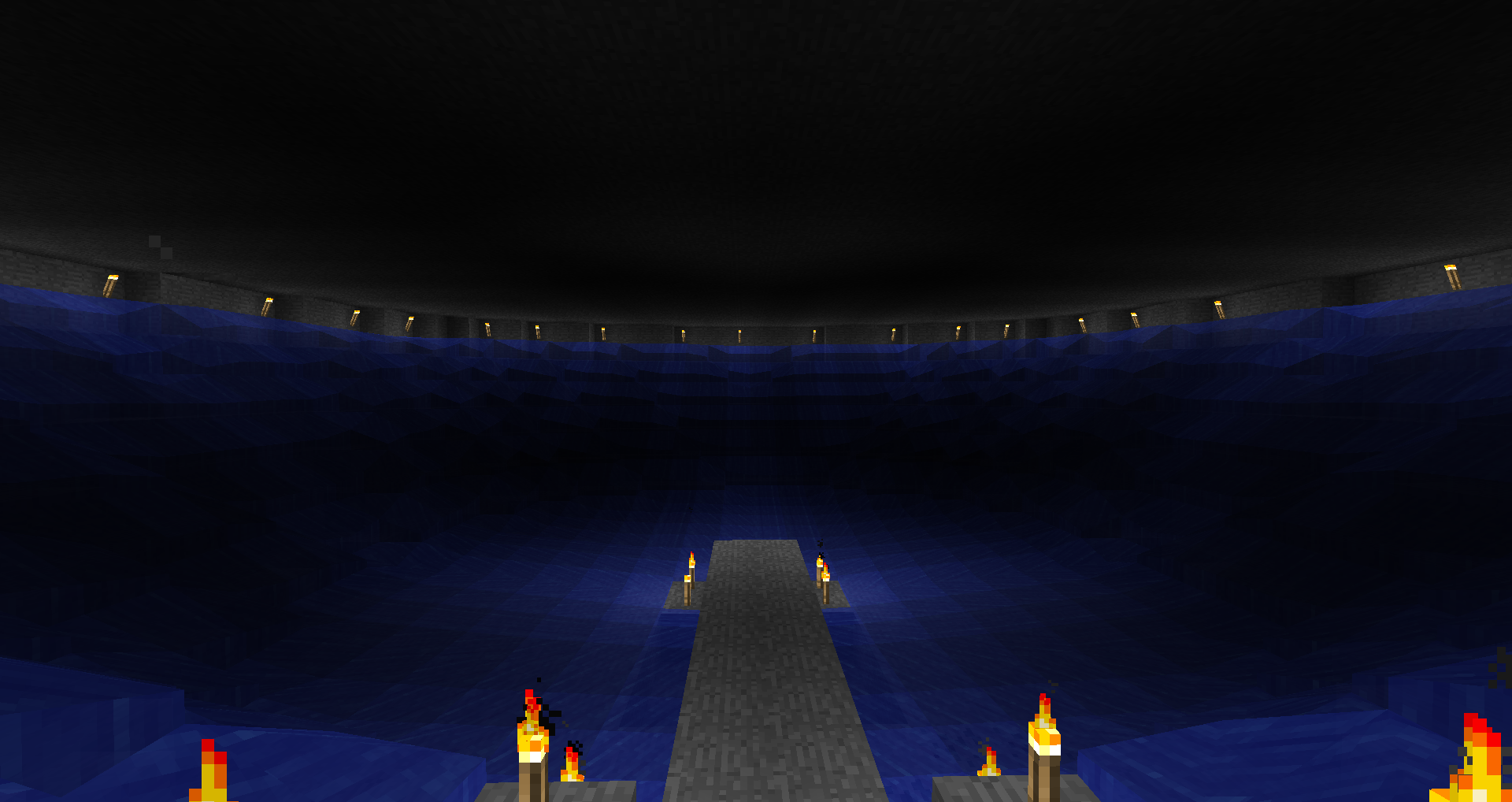 A large, dark arena with a central walkway and lit torches along the edges.