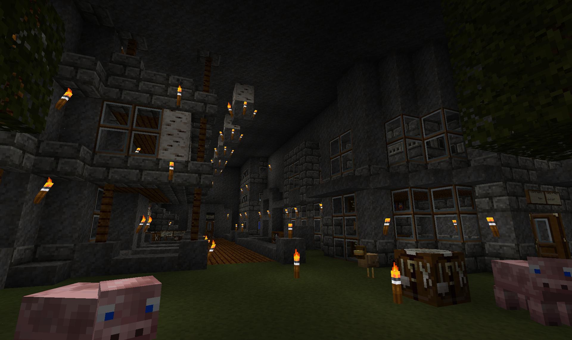 A large stone building with many windows and a grassy area in front, featuring several pigs and lit torches.