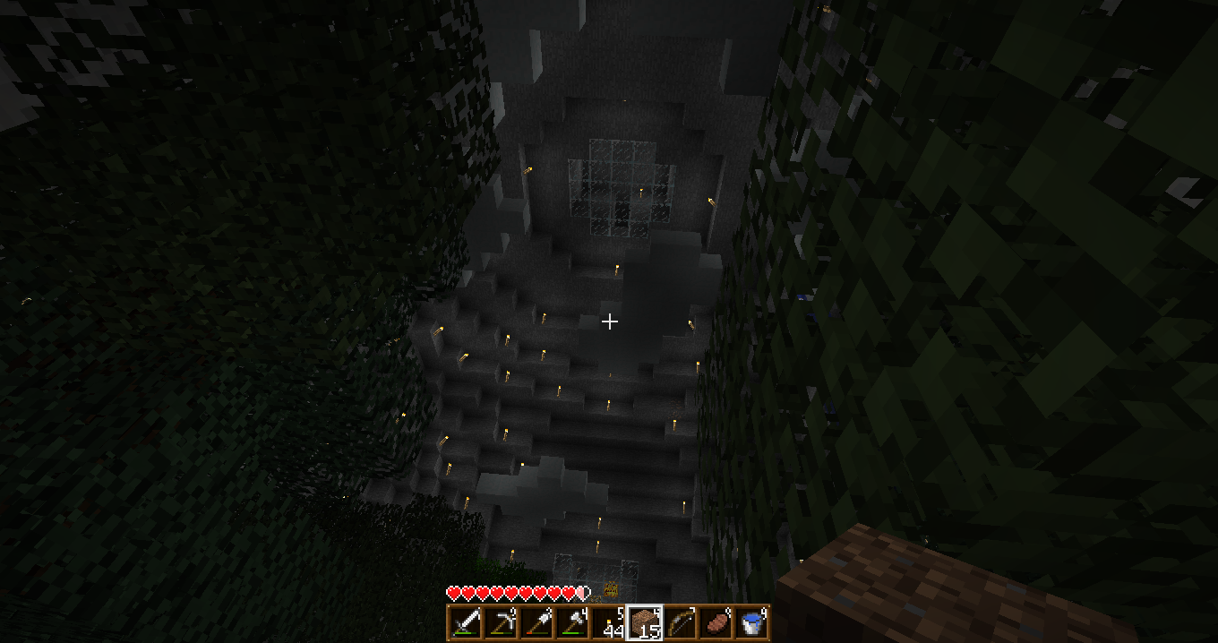 A dark and mysterious cave with a small amount of light coming from the top, surrounded by trees and rocks.
