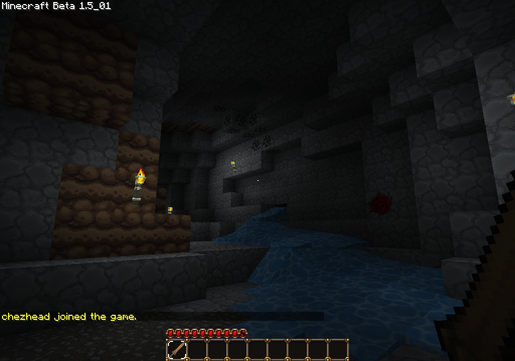 A dark cave with a small pool of water and a few blocks of dirt, with a player's inventory visible at the bottom.