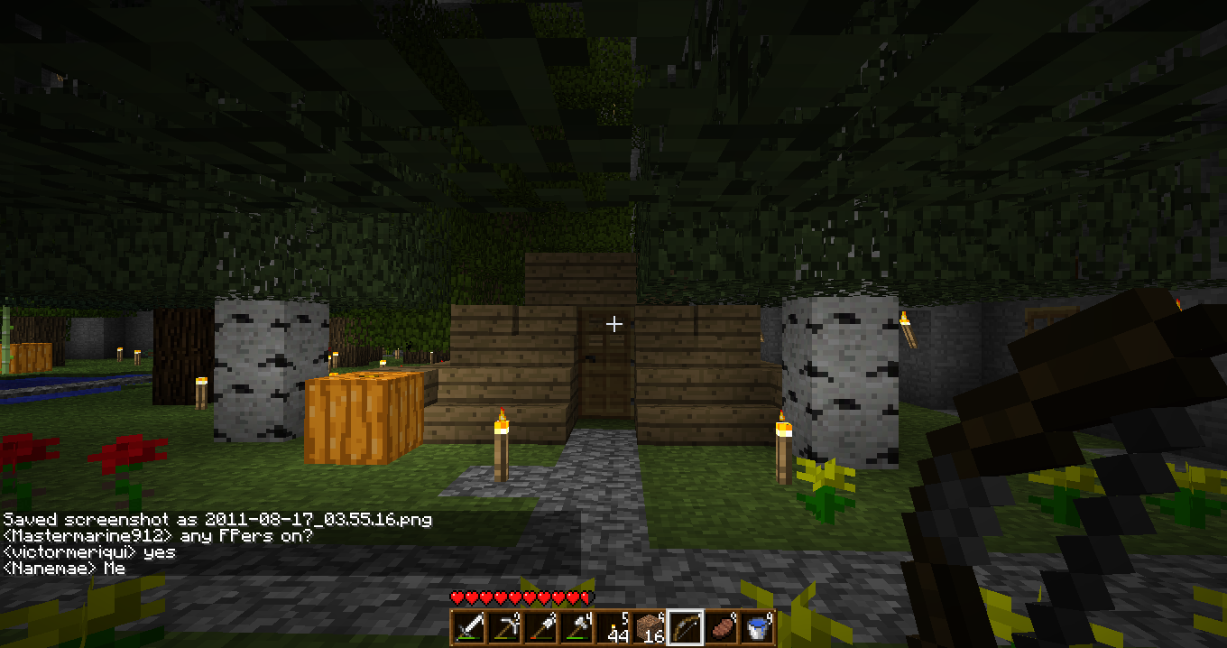 A screenshot of a Minecraft base with a stone wall and wooden gate, surrounded by trees and grass.