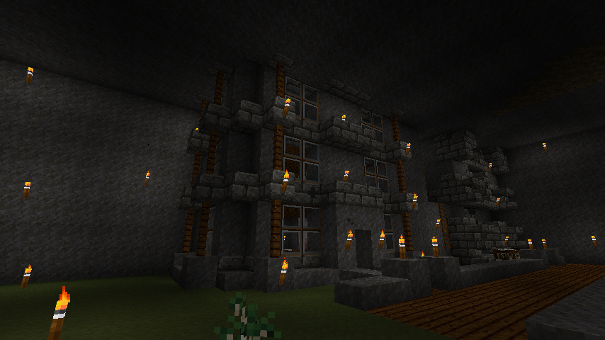 A large stone building with many windows and torches, surrounded by a grassy area with a few trees.
