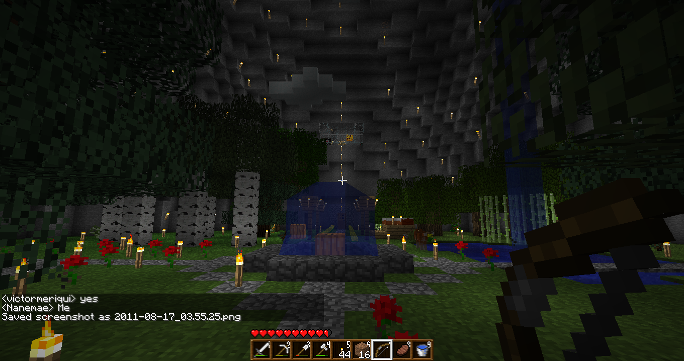 A large, dark cave with a blue structure in the center and red flowers around it.
