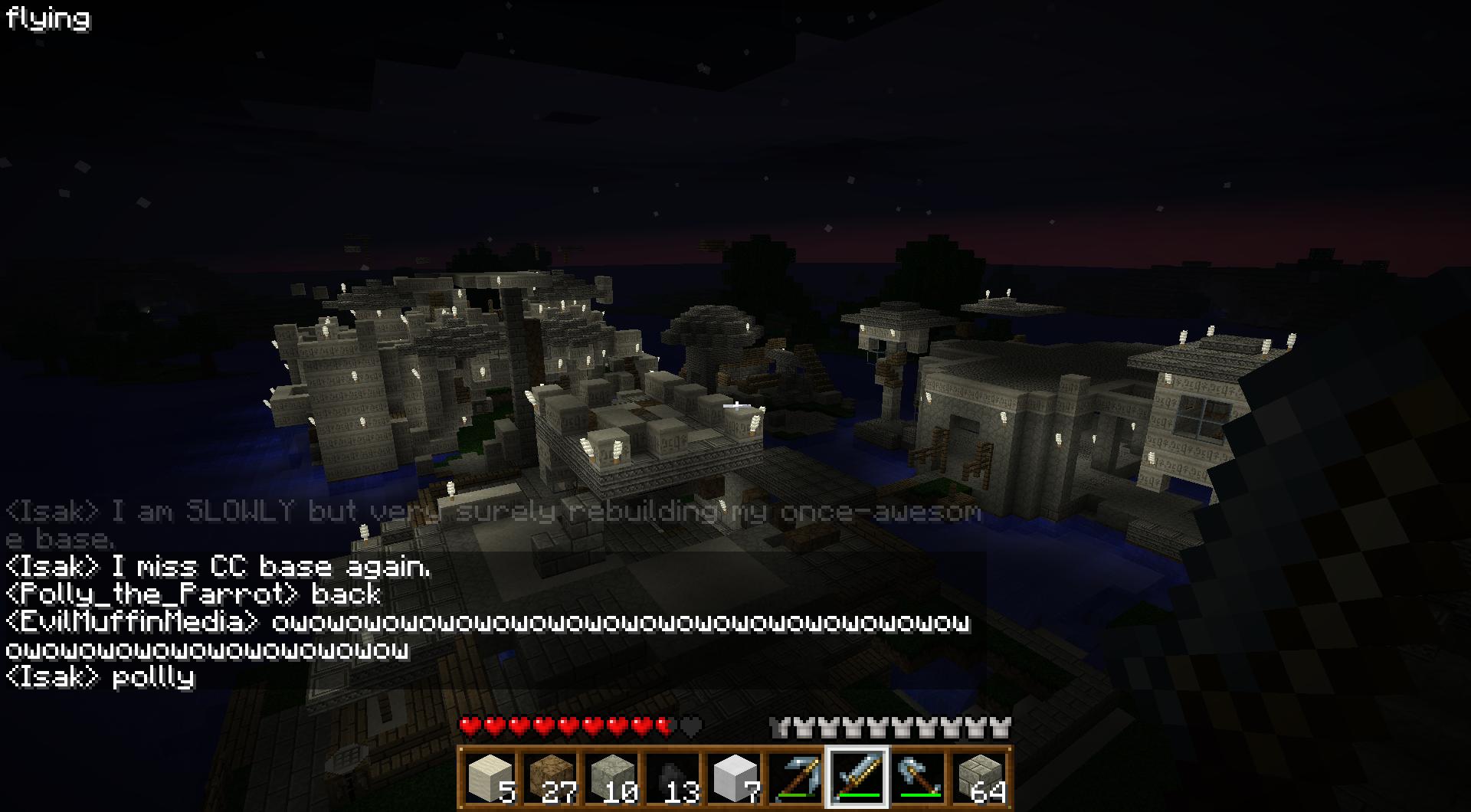 A nighttime screenshot of a large, white, castle-like structure with a moat, surrounded by water and trees. The chat window is open, displaying messages from players.